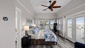 A bedroom with a bed, bedside tables, a ceiling fan, and large windows. - Waterfront luxury! Free bikes & kayaks! Great fishing! Bike to the beach! (Galveston)