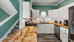 A kitchen with white cabinets, a granite countertop, and a stainless steel refrigerator. - Waterfront luxury! Free bikes & kayaks! Great fishing! Bike to the beach! (Galveston)