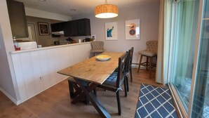 A modern kitchen with dark cabinets, a wooden dining table, and a hanging light fixture.