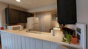 A modern kitchen with white cabinetry, a built-in microwave, a refrigerator, and a sink. There is a potted plant on the counter and a framed picture on the wall.