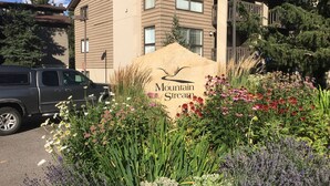 A building with a sign reading "Mountain Stream" surrounded by a variety of flowers and plants.