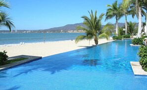 Vista de la piscina con playa y montañas al fondo.