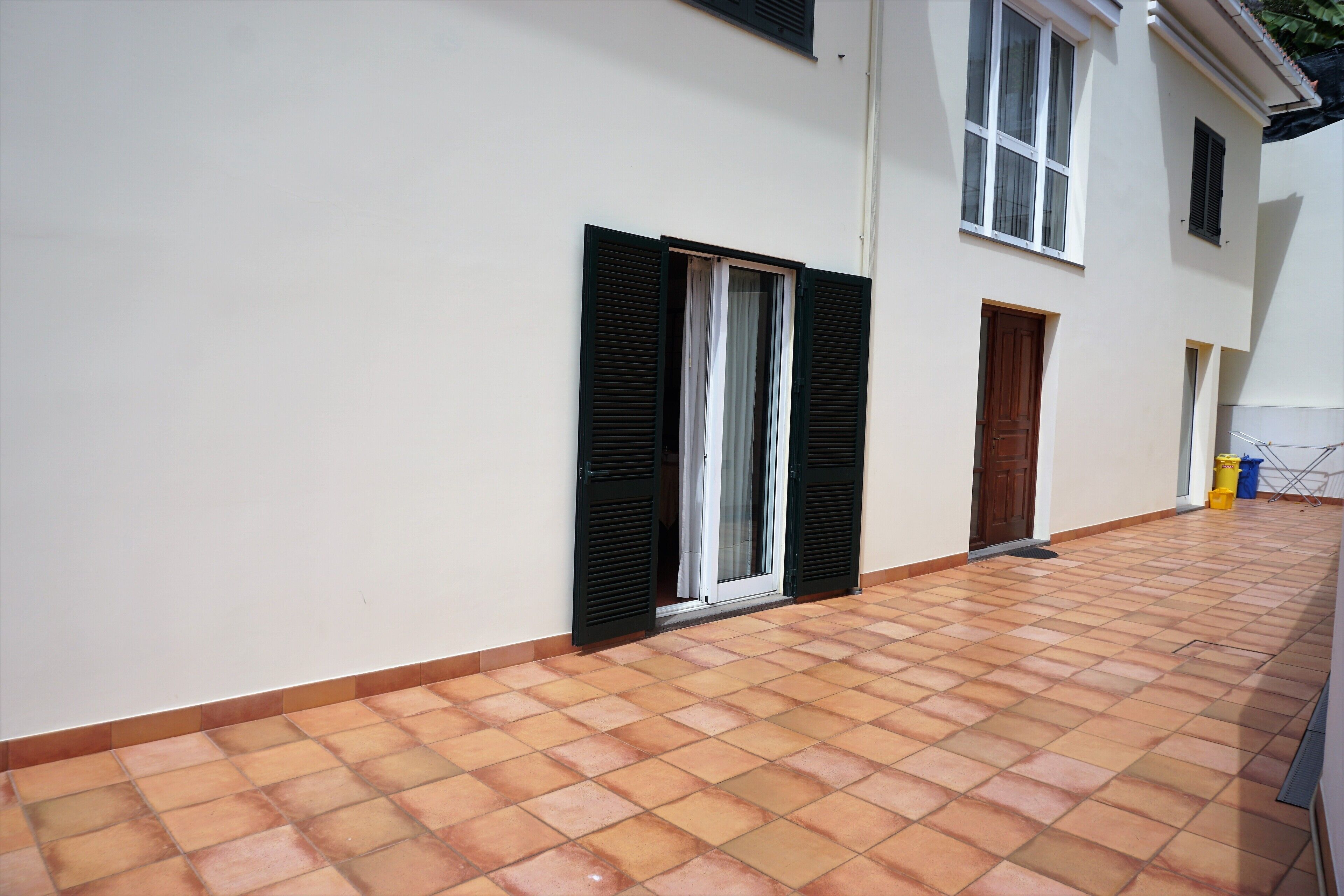 A building with a tiled patio, a door, and windows with shutters.