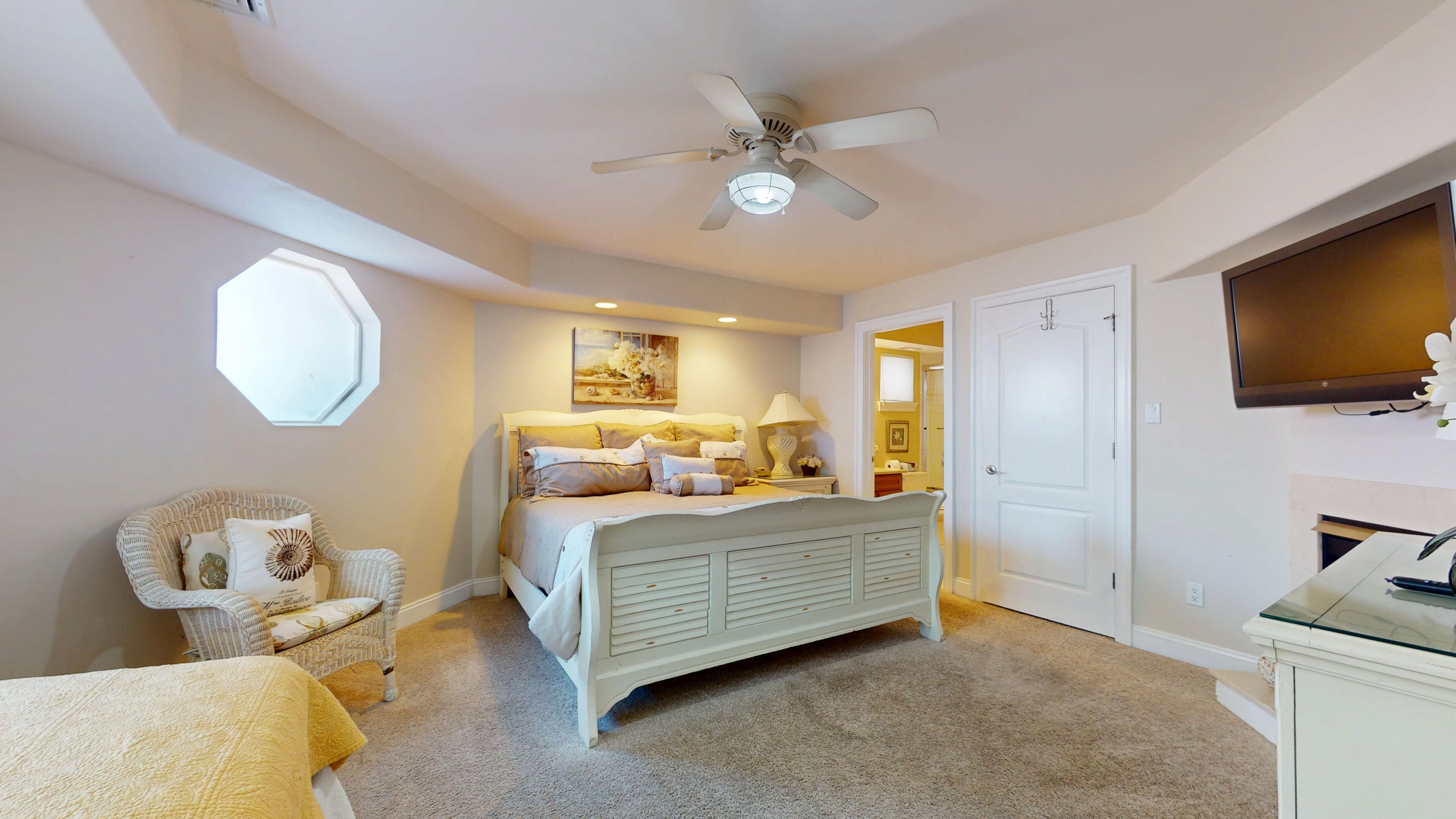 A bedroom with a bed, a chair, a ceiling fan, a window, and a door.