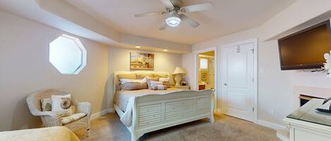 A bedroom with a bed, a chair, a ceiling fan, a window, and a door.
