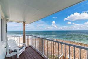 Une terrasse en bois avec une balustrade blanche donnant sur une plage et l’océan.