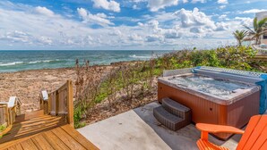 Eine Holzterrasse führt zu einem Strand mit Whirlpool und orangefarbenen Stühlen.