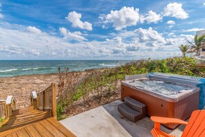 Una terraza de madera que da a una playa, con un jacuzzi y sillas anaranjadas.