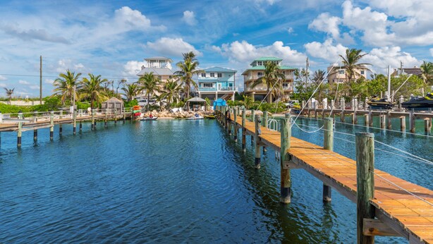 A waterfront property with a wooden dock extending into a calm body of water, surrounded by palm trees and residential buildings with balconies. - Heaven Can't Wait:  ON the BEACH!! Heated pool + hot tub, private dock. 7BR/5BA (Stuart)
