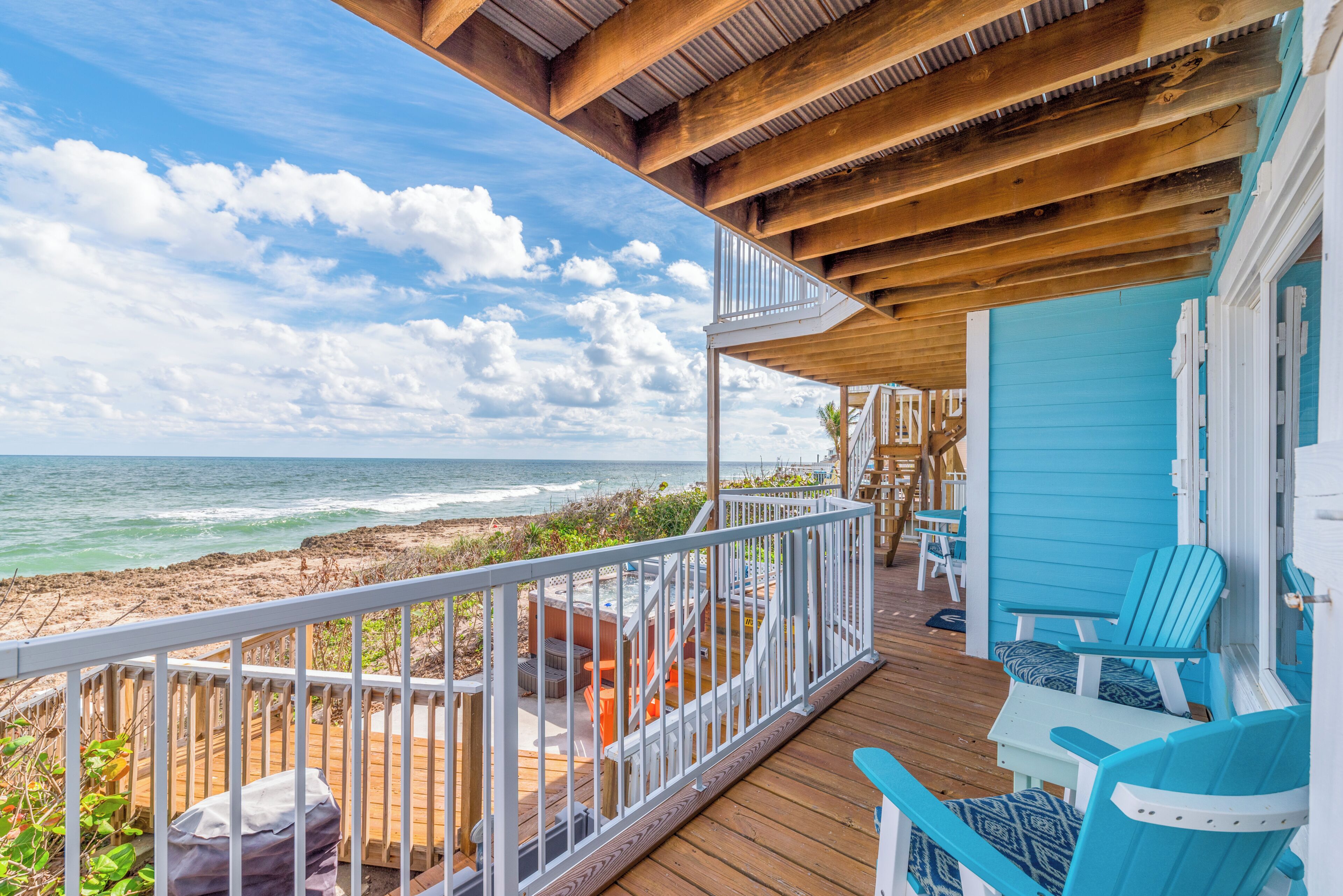 A wooden deck with a view of the ocean, outdoor seating, and a covered area.