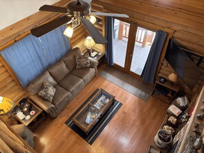 Interior acogedor de una cabaña con ventilador de techo, pisos de madera, sofá, mesa de centro y televisor.