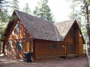 A log cabin with a steeply pitched roof, a front porch, and a small front yard.