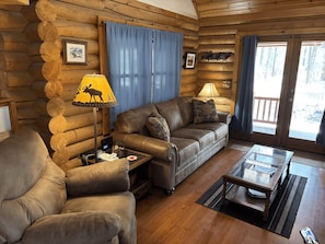 A log cabin interior with a leather sofa, a coffee table, and a lamp with a moose design. - Log Cabin on National Forest - Quiet, Relaxing, Serene. (Pinetop)