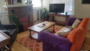 A living room with a brick fireplace, a television on a wooden stand, a purple sofa, and a patterned rug. - Three Bedrooms Two Baths sleeps 6 - Walking distance to Downtown Paso Robles (Paso Robles)