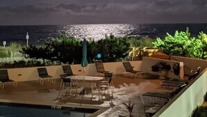A pool area with lounge chairs and a view of the ocean under a bright moon.
