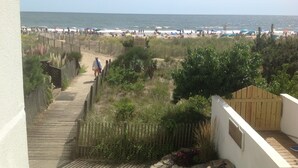 A beach view with a wooden boardwalk leading to the shore, surrounded by vegetation and a fence.