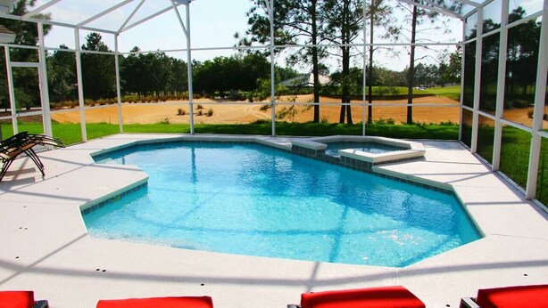 A swimming pool with a glass enclosure, red lounge chairs, and a view of a golf course. - Immaculate Spacious Villa.No rear neighbors,Games Room,office,Large pool,hot spa (Davenport)