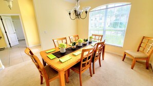 A dining room with a wooden table set for six, surrounded by chairs, with a chandelier above and a window with blinds to the right. - Immaculate Spacious Villa.No rear neighbors,Games Room,office,Large pool,hot spa (Davenport)
