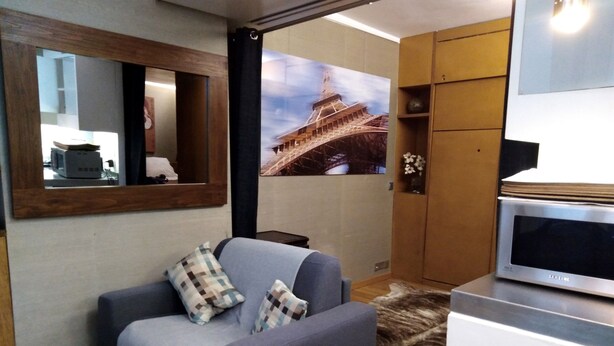 Een moderne woonkamer met een grijze bank, een houten kast, een flatscreen televisie en een groot poster van de Eiffeltoren.