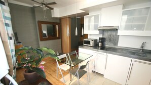 Een moderne keuken met witte kastjes, een magnetron en een koffiezetapparaat. Er staat een eettafel met stoelen en een potplant.