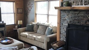 A cozy living room with a stone fireplace, wooden ceiling beams, and a comfortable sofa. - Cozy Cabin Secluded in the Woods.  Wildlife Abundant.  Not a neighbor in sight! (Harshaw)