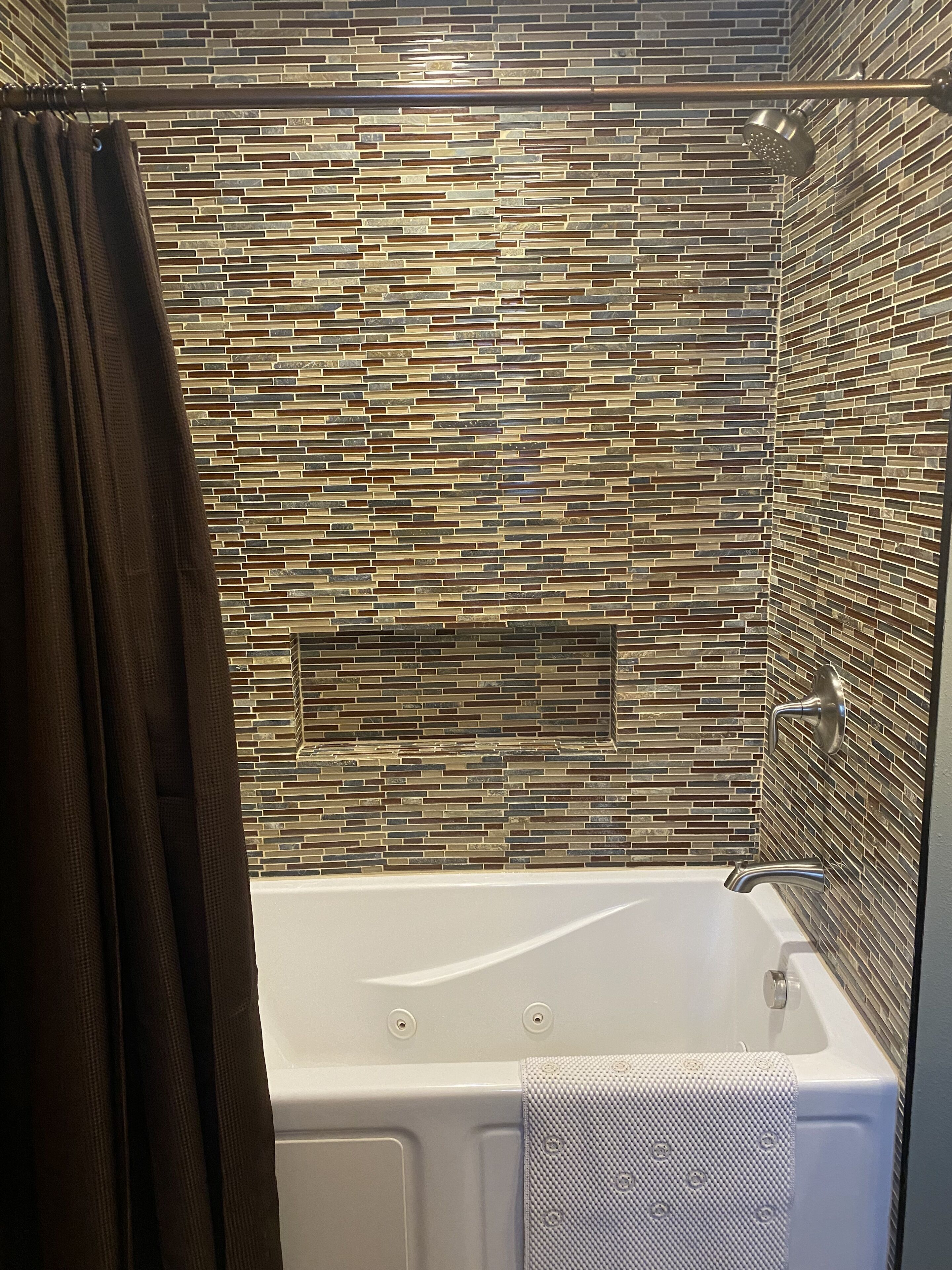 A modern bathroom with a mosaic tile wall, a bathtub, and a showerhead.