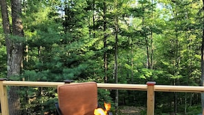 A deck with a metal fire pit, a cushioned chair, and a wooden railing. - Cozy Cabin Secluded in the Woods.  Wildlife Abundant.  Not a neighbor in sight! (Harshaw)