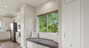A kitchen with white cabinetry, a built-in bench with cushions, and a window with a view of greenery. - 808 B xxxxxxxxxxxxxx (Austin)