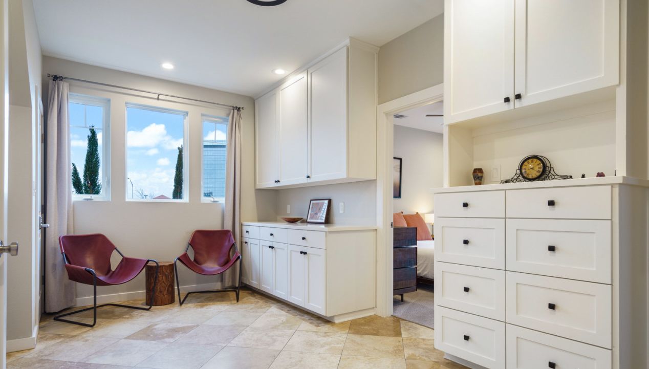A modern interior with a kitchen area, white cabinets, a dining table with chairs, and a view of the outside.