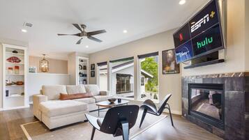 A modern living room with a sofa, chairs, a fireplace, and a mounted TV displaying streaming services.