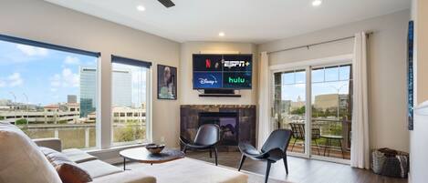 A modern living room with a sofa, chairs, a fireplace, and a TV displaying streaming services.