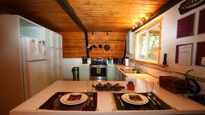 A compact kitchen with wooden ceiling, white cabinets, and a central island with a dining setup. - RIVER IN YOUR FRONT YARD!/Suspended Fireplace/Perfect for Families & Groups/PETS (Red River)