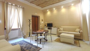 A living room with a sofa, a coffee table, a TV, and a coat rack. - Rome Historic Core Apartment - Between Colosseum & Termini – A/C, Wi-Fi, Netflix (Roma)
