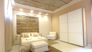 A bedroom with a stone wall, a bed with white linens, a white chair, and a large wardrobe. - Rome Historic Core Apartment - Between Colosseum & Termini – A/C, Wi-Fi, Netflix (Roma)