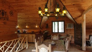 A wooden cabin interior with a dining table, chairs, a chandelier, and a kitchen area. - Lakefront on 31 acres, Kayaks, boat, Hiking, Fishing, Private Lake. (Paupack)
