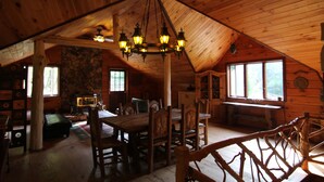 A wooden cabin interior with a dining area, stone wall, and large windows. - Lakefront on 31 acres, Kayaks, boat, Hiking, Fishing, Private Lake. (Paupack)