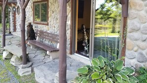 A stone building with a wooden porch, a bench, and a large window. - Lakefront on 31 acres, Kayaks, boat, Hiking, Fishing, Private Lake. (Paupack)