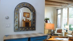 Une pièce avec un grand miroir, une commode bleue, une table en bois avec une lampe et une fenêtre avec des rideaux.