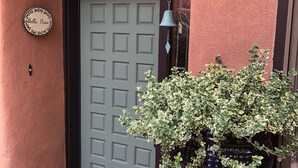 Une porte ornée d’une cloche décorative, un pot de fleurs et une enseigne sur laquelle on peut lire « Bella Casa ».