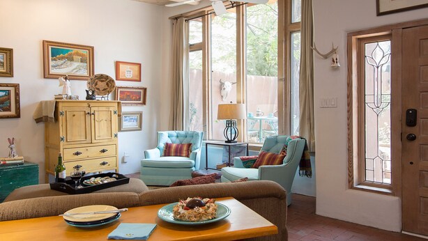 A cozy living room with a wooden cabinet, two armchairs, a dining table with plates and a bottle, and a window with curtains.