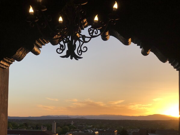 A sunset view through a dark, ornate window frame with a chandelier.