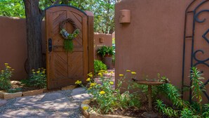 A wooden gate with a wreath, a potted plant, and a birdbath in a garden area.