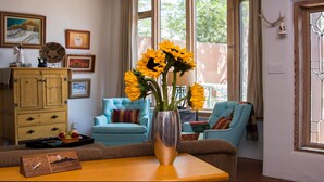 A living room with a vase of sunflowers on a table, a blue sofa, and a wooden cabinet with framed pictures.