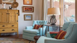 A cozy living room with a light blue armchair, a matching sofa, a wooden cabinet, and a table with a lamp.
