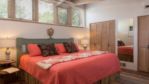 Une chambre à coucher comprenant un lit, une table de chevet, une lampe, une fenêtre avec des stores, un miroir et une armoire.