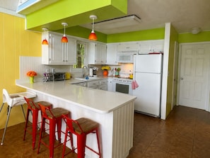 A kitchen with white cabinets, a central island with stools, a microwave, and a refrigerator. - Lakefront 🛶 • Spa ♨️ • Firepit 🔥 • Boating 🚣‍♂️ • Game Rm 🎮 • Fishing 🎣 • Sunsets 🌅 (Poconos Lake)