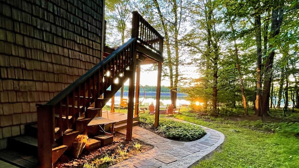 A wooden staircase leading to a deck with outdoor seating, surrounded by a lush garden and a lake view. - Lakefront 🛶 • Spa ♨️ • Firepit 🔥 • Boating 🚣‍♂️ • Game Rm 🎮 • Fishing 🎣 • Sunsets 🌅 (Poconos Lake)