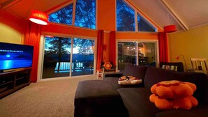 A living room with a large TV, a sofa, and a plush toy. - Lakefront 🛶 • Spa ♨️ • Firepit 🔥 • Boating 🚣‍♂️ • Game Rm 🎮 • Fishing 🎣 • Sunsets 🌅 (Poconos Lake)