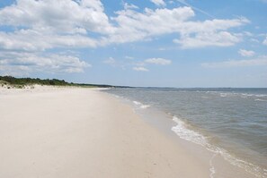 A wide sandy beach with gentle waves, a clear sky, and a distant pier.