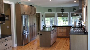 A spacious kitchen with wooden cabinets, a stainless steel refrigerator, and a large island with drawers. - Family vacation retreat w/ In-ground Pool with private Chesapeake Bay access! (Cape Charles)